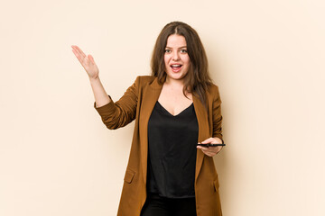 Young curvy woman holding a phone receiving a pleasant surprise, excited and raising hands.