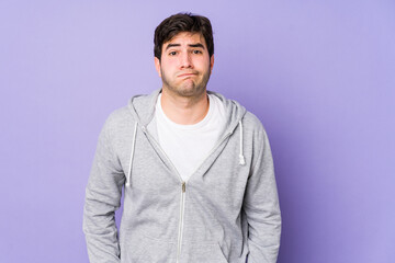 Young man isolated on purple background blows cheeks, has tired expression. Facial expression concept.