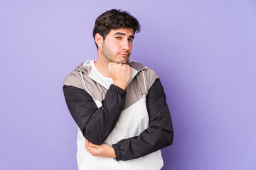 Young man isolated on purple background suspicious, uncertain, examining you.