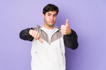 Fototapeta premium Young man isolated on purple background showing thumbs up and thumbs down, difficult choose concept