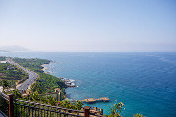 Naklejka premium An empty asphalt road winds along the breathtaking scenic coastline on a sunny summer day. A spectacular shot of a coastal road overlooking clear blue skies and the calm Mediterranean Sea.