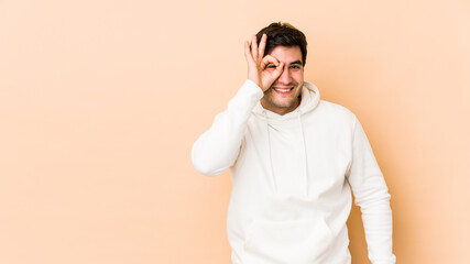 Young man isolated on beige background excited keeping ok gesture on eye.