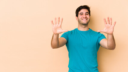 Young man isolated on beige background showing number ten with hands.