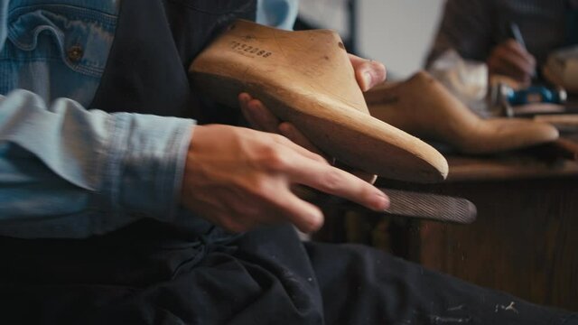 Close up shoemaker polishes wooden mold for shoes in workshop, man making leather boots, craft industry handmade