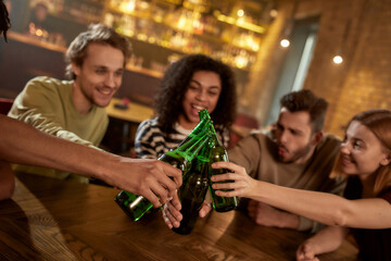 Cheers. A group of happy friends in the bar watching sports match on TV together, drinking beer, clinking bottles and cheering for team. People, leisure, friendship and entertainment concept