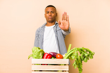 Young farmer man isolated on a beige background standing with outstretched hand showing stop sign, preventing you.