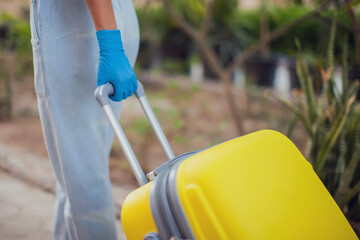 Travel and coronavirus concept. Woman with medical gloves holding luggage outdoor.