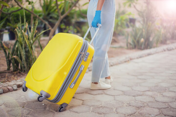 Travel and coronavirus concept. Woman with medical gloves holding luggage outdoor.