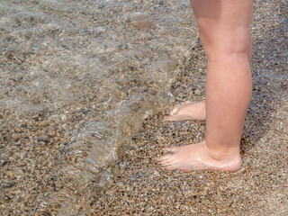 Small baby feet close-up on the sand of the sea beach. Sea water washes the feet. Happy childhood. Rest at the sea. Summer sunny day. Copy space.
