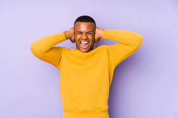 Fototapeta na wymiar Young latin man isolated on purple background covering ears with hands trying not to hear too loud sound.