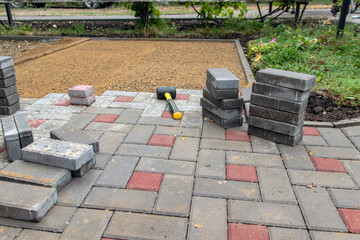 A worker installs paving slabs in the yard. Laying gray concrete paving slabs in the courtyard of the house on a sandy foundation. Selective focus.