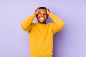 Young latin man isolated on purple background laughs joyfully keeping hands on head. Happiness concept.