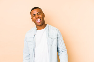 Fototapeta premium Young latin man isolated on beige background funny and friendly sticking out tongue.