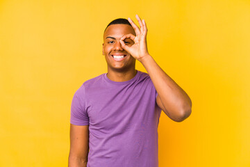 Fototapeta premium Young latin man isolated on yellow background excited keeping ok gesture on eye.