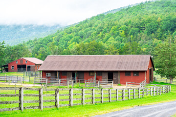 Obraz premium Red Barn Surrounded by Green Mountains Covered with Fog.