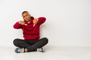 Young latin man sitting on the floor isolated showing thumb down and expressing dislike.
