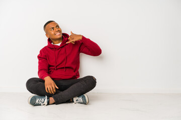 Young latin man sitting on the floor isolated showing a mobile phone call gesture with fingers.