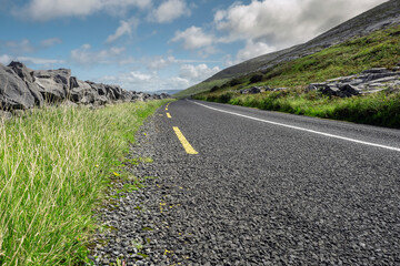 Small asphalt road by Atlantic ocean, Burren National geo park, Ireland. Nobody, Warm sunny day. Beautiful cloudy blue sky. Part of Wild Atlantic Way. Low angle, selective focus.