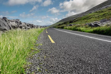 Foto op Plexiglas Atlantische weg Small asphalt road by Atlantic ocean, Burren National geo park, Ireland. Nobody, Warm sunny day. Beautiful cloudy blue sky. Part of Wild Atlantic Way. Low angle, selective focus.