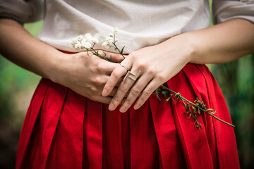 Lady wearing red skirt and silver rings holds flower