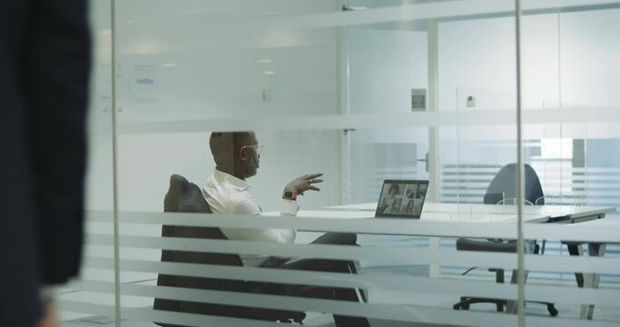 Businessman in empty meeting room using Video Conferencing technology on laptop talking to colleagues working from home