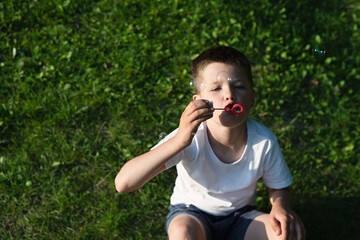 Fototapeta premium boy will invent soap bubbles, sitting on green grass in park