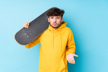 Young arab skater man isolated shrugs shoulders and open eyes confused.