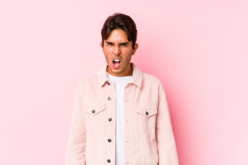 Young caucasian man posing in a pink background isolated screaming very angry and aggressive.