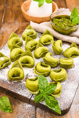 Tortellini e tortelloni typical dishes emilia italy. Food background with homemade raw Italian tortelloni and ingredients for green pesto on wooden background . High angle view. Copy space.