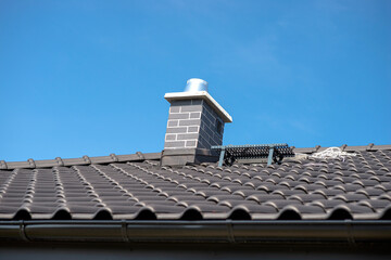 The roof of a single-family house covered with a new ceramic tile in anthracite against the blue...