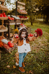  little girl in a Fox costume and with a Fox tail stands at the autumn fair 