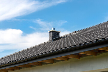 The roof of a single-family house covered with a new ceramic tile in anthracite against the blue...