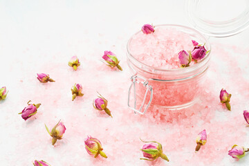 Pink aroma bath salt in a glass jar decorated with dried rose flowers on pink bath salt background. Spa, skincare concept. Selective focus