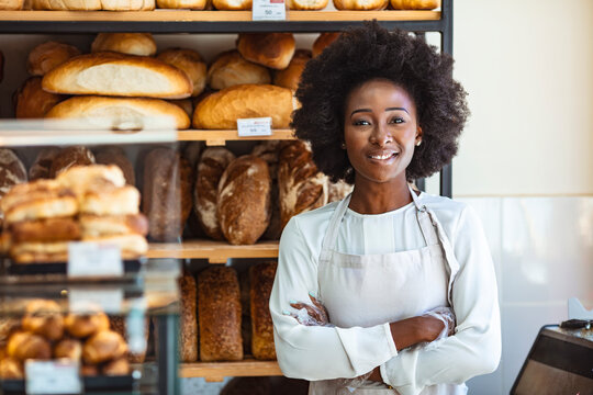 Portrait of positive African American young woman working in own Bakery shop, looking at camera with toothy smile. Pretty baker smiling at camera. Small Bakery shop owner standing in front of store
