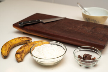 Coconut and banana cookies preparation drizzled with melted chocolate. Ingredients displayed. 