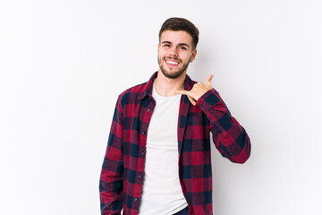 Young caucasian man posing in a white background isolated showing a mobile phone call gesture with fingers.