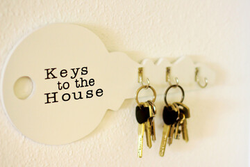 Bunch of keys hanging on a holder on a white wall, wooden key holder on light wall