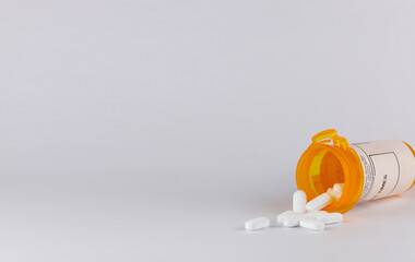 pill bottle lying on its side with white tablet pills spilling out on a white background with copy space in landscape format