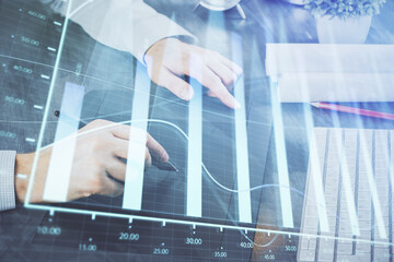 Double exposure of man's hands holding and using a phone and financial graph drawing. Analysis concept.