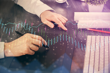 Double exposure of man's hands holding and using a phone and financial graph drawing. Analysis concept.