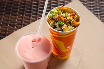 pink milkshake with juice in a transparent glass next to sweet colorful popcorn