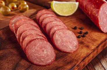 Sliced smoked salami on cutting board with cubs of cheese and olives