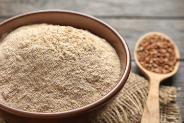 Buckwheat flour in bowl and spoon with seeds on wooden table, closeup