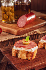 Delicious canapes with salami, cream cheese, olives and tomatos on a wooden background - Close-up
