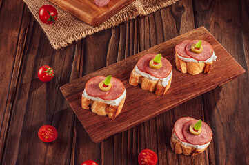 Delicious canapes with salami, cream cheese, olives and tomatos on a wooden background