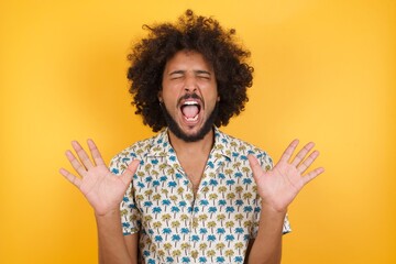 Emotive Young man with afro hair over wearing hawaiian shirt standing over yellow backgrou laughs loudly, hears funny joke or story, raises palms with satisfaction, being overjoyed, amused by friend. 
