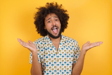 Young man with afro hair over wearing hawaiian shirt standing over yellow background celebrating crazy and amazed for success with arms raised and open eyes screaming excited. Winner concept