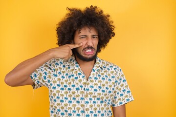 Fototapeta na wymiar Young man with afro hair over wearing hawaiian shirt standing over yellow background pointing unhappy to pimple on forehead, ugly infection of blackhead. Acne and skin problem