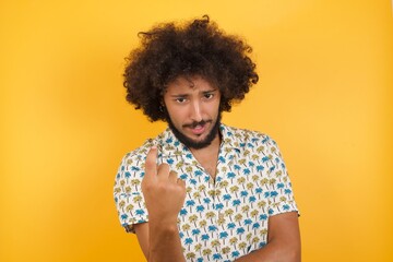 Young man with afro hair over wearing hawaiian shirt standing over yellow background Beckoning come here gesture with hand inviting welcoming happy and smiling