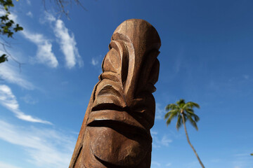 Wood carved tiki under a blue sky and palm trees on a French Polynesia tropical island
